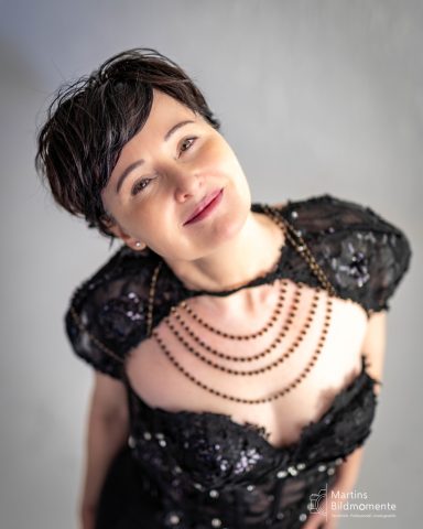 Frau mit kurzem Haar in einem eleganten, glitzernden Kleid mit Halskette, lächelnd.