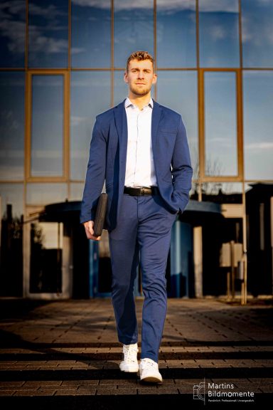 Mann in Anzug und Sneakers geht selbstbewusst auf einer Straße mit reflektierenden Glasfassaden.