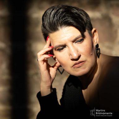 Eine nachdenkliche Frau mit kurzen, dunklen Haaren, die einen schwarzen Pullover trägt.